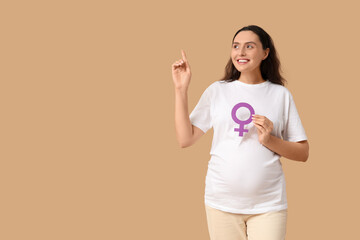 Young pregnant woman with gender symbol pointing at something on beige background