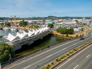 Elevated view of a modern pedestrian bridge over a waterway, connecting Whangarei  city streets. Cars parked below, and a person walking.  Northland, New Zealand
