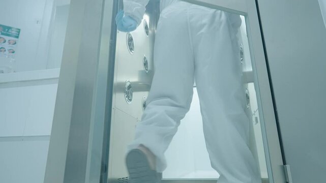 scientist in white protection suit walking through the air shower blowing disinfect machine to clean before working inside the lab, hygiene standard routine procedures before entering laboratory