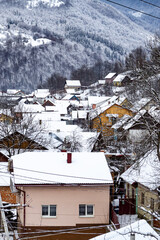 Different houses in snowy mountains during winter, surrounded by snow-covered trees. Pink house with snow covered roof. A peaceful scene. Vertical photo