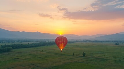 Obraz premium Hot Air Balloon at Sunrise Over Green Fields and Mountains