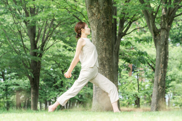 Naklejka premium 森・公園でパークヨガ・ヨガ・ピラティス・ストレッチをする若いアジア人女性 