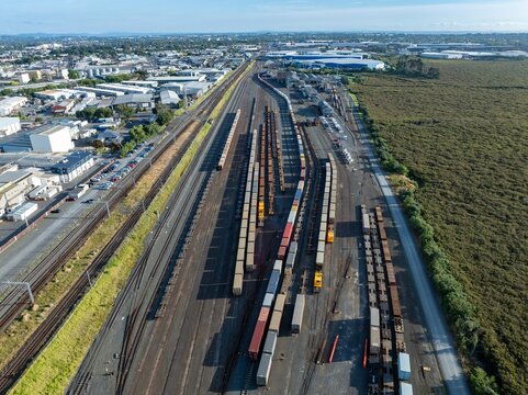 Aerial view of a busy rail yard. Freight cars and containers are parked along multiple tracks. Industrial buildings and city are visible in the background. PENROSE, AUCKLAND, NZ