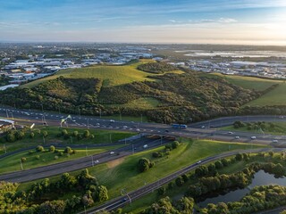 High-angle view of a highway intersecting with a grassy area and a body of water. Traffic flows smoothly through the urban landscape. MT WELLINGTON, AUCKLAND, NZ
