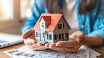 Woman's hands hold a model house with rental contracts nearby