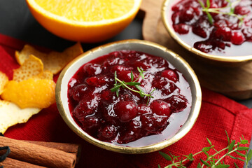 Tasty cranberry sauce in bowls, orange, thyme and cinnamon on table, closeup