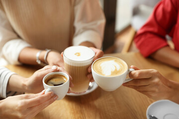 Women with cups of delicious coffee drinks at wooden table in cafe, closeup
