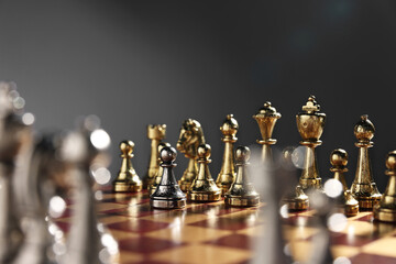 Silver pawn in front of golden chess pieces on chessboard against grey background, closeup....