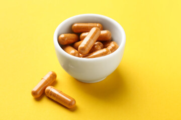 Turmeric capsules in bowl on yellow background, closeup
