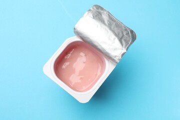 Delicious chocolate yogurt in plastic cup on light blue background, top view