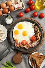 Tasty fried eggs with bacon and mushrooms served on grey table, flat lay