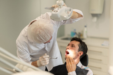 Elderly male doctor dentist examining teeth of adult male patient before treatment in office
