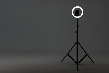 Ring lamp with smartphone on grey background, space for text