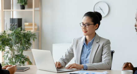 A woman in a business suit sits at a desk with a laptop in front of her