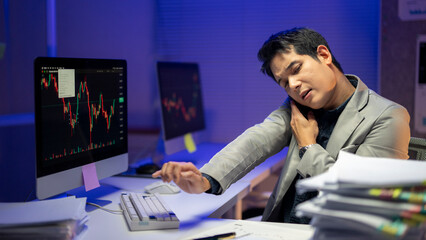 Fototapeta premium A man in a suit is hunched over a computer, rubbing his neck