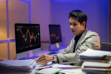 A man in a suit is sitting at a desk with two computer monitors