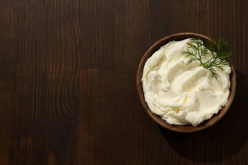 Philadelphia cheese in a wooden plate on a brown background.