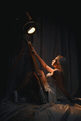 Beautiful blonde woman in white skirt with corset posing with theatrical retro spotlight on white fabric background in the dark.