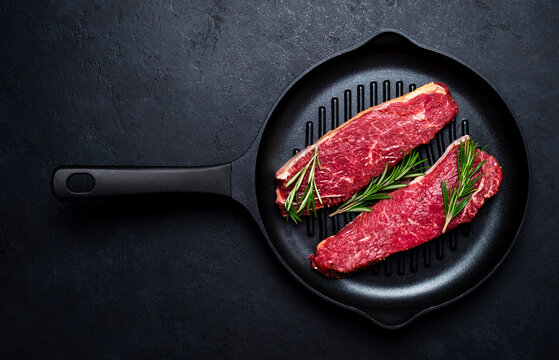 Raw beef sirloin steaks with medium mamory with rosemary on grill pan. Black background, top view