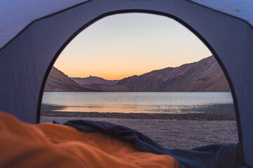 lake sight from a tent at sunset sleeping in an orange sleeping bag in Cajón del Maipo, Chile 