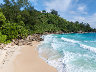 The gentle surf of the turquoise ocean meets the sandy beach. Seychelles, Mahe. Anse Intendance beach.