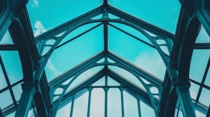 Close-up photo of a blue glass roof with black metal frames, featuring a geometric shape against a sky background.