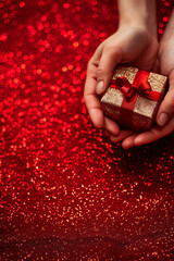  Hand holding a gift box on shimmering red glitter background for valentines day