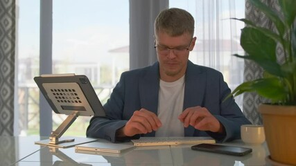 A young teacher in glasses leads an online webinar, smiling as he explains the material. He switches slides on his tablet, displaying examples and illustrations to deepen understanding of the topic.