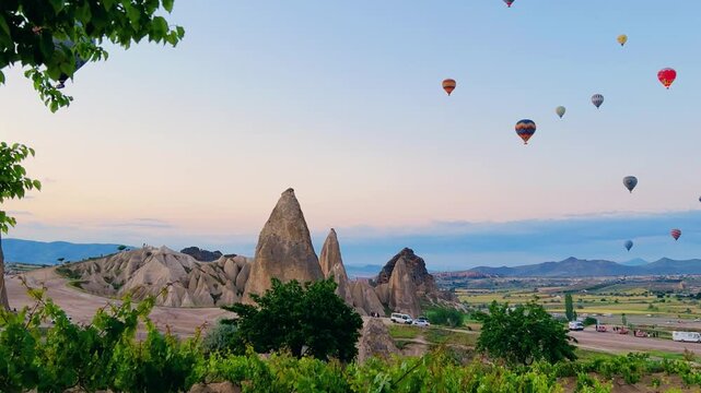 Goreme, Turkey, May 7, 2024: Colorful balloons in Cappadocia fly in the sky over deep canyons at dawn. A lot of balloons with tourists hover and fly in the blue sky above the valley of rocks. 4К