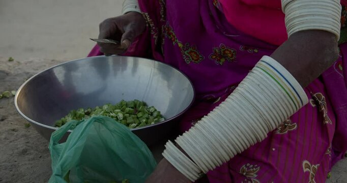 Closeup slow motion of a Sindhi woman preparing okra for cooking at sunset in Thar dessert, Pakistan