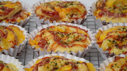 A group of salty bread is served in a paper cup with smoked beef filling, orange cheddar and topped with mayonnaise, tomato sauce, and parsley which is placed on a cooling rack with a white background