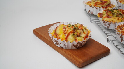 A group of salty bread is served in a paper cup with smoked beef filling, orange cheddar and topped with mayonnaise, tomato sauce, and parsley which is placed on a cooling rack with a white background