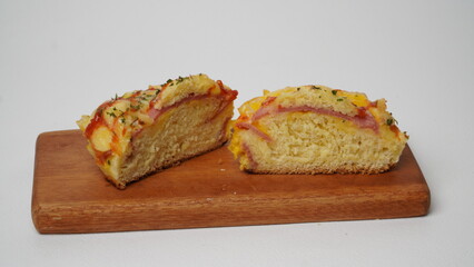 A half salty bread is served in a paper cup with smoked beef filling, orange cheddar and topped with mayonnaise, tomato sauce, and parsley which is placed on a wooden plate with a white background
