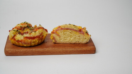 A half salty bread is served in a paper cup with smoked beef filling, orange cheddar and topped with mayonnaise, tomato sauce, and parsley which is placed on a wooden plate with a white background