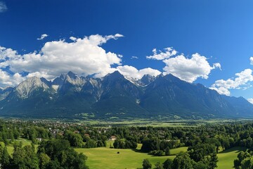 Fototapeta premium panoramic view of the Alps, with majestic mountains in the background and lush green meadows below. The sky is blue with fluffy white clouds adding to its picturesque charm.