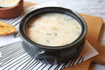 Creamy chicken soup served in a black bowl with toast and lemon
