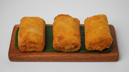 Three American rissols containing boiled eggs, smoked beef and mayonnaise are served on a brown wooden board covered in banana leaves with a white background and base (isolated white).