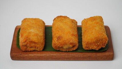Three American rissols containing boiled eggs, smoked beef and mayonnaise are served on a brown wooden board covered in banana leaves with a white background and base (isolated white).