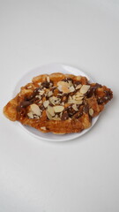 A croffle topped with chocolate jam and a sprinkling of sliced ​​almonds served on a white plate and placed on a white base and background (isolated white).