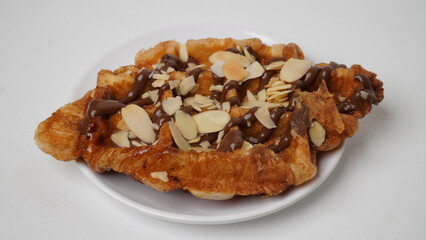 A croffle topped with chocolate jam and a sprinkling of sliced ​​almonds served on a white plate and placed on a white base and background (isolated white).
