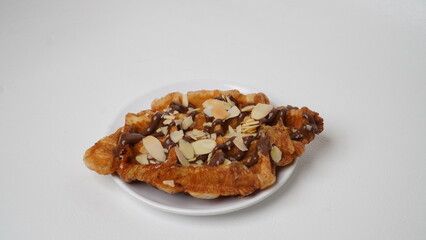 A croffle topped with chocolate jam and a sprinkling of sliced ​​almonds served on a white plate and placed on a white base and background (isolated white).