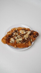 A croffle topped with chocolate jam and a sprinkling of sliced ​​almonds served on a white plate and placed on a white base and background (isolated white).