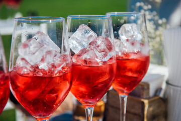 A wine glass filled with ice cubes with red wine, pink vermouth, and a red drink. Cocktail preparation at a party, Iced wine, selective focus