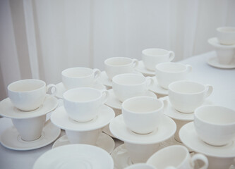 Lots of empty tea or coffee cups on a white table against a white wall, space for text.  Organization of events, catering, catering, beautiful white and gray background