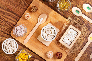 Dietary supplements, vitamins and minerals such as vitamin d3, a, b, c, e, k, magnesium, zinc and multivitamin pills in small plates on wooden desk on a wooden background in sunshine. Rustic style.