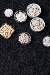 Dietary supplements, many vitamins and minerals in small plates and jars on black background from above. Big amount of white colored pills and nutritional supplements, top view. Healthy lifestyle