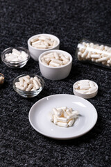 Dietary supplements, many vitamins and minerals in small plates and jars on black background from above. Big amount of white colored pills and nutritional supplements, top view. Healthy lifestyle