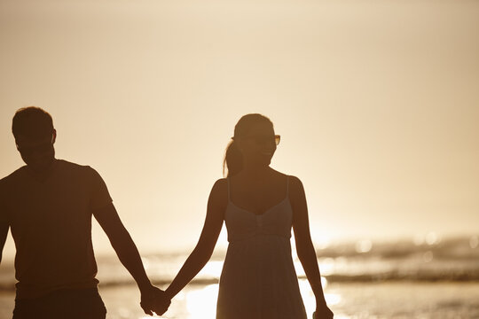 Walking, love or couple holding hands at beach for valentines day, sunset or romance. Summer vacation, silhouette or people bonding on holiday at sea in Spain for romantic honeymoon or travel date