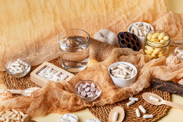 Glass of water, many food supplements in forms of tablets, pills and capsules on beige background in rustic style. Dietary supplements, vitamins and minerals for healthy lifestyle.