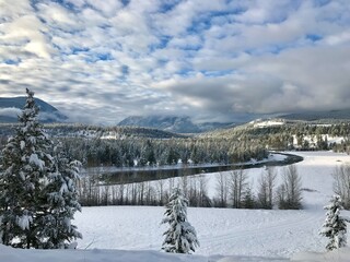 winter landscape with snow covered trees, cloudy sky, winding river 